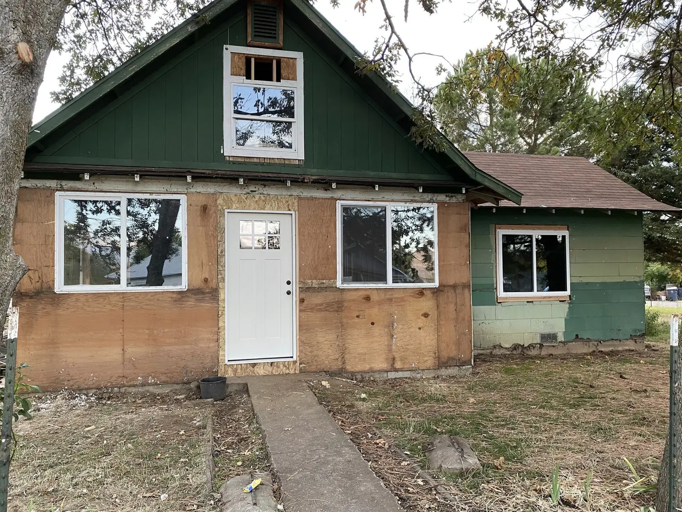 Siding repair in progress on a green home, lower walls stripped to the sheathing, by Next Gen Contracting in Southern Oregon
