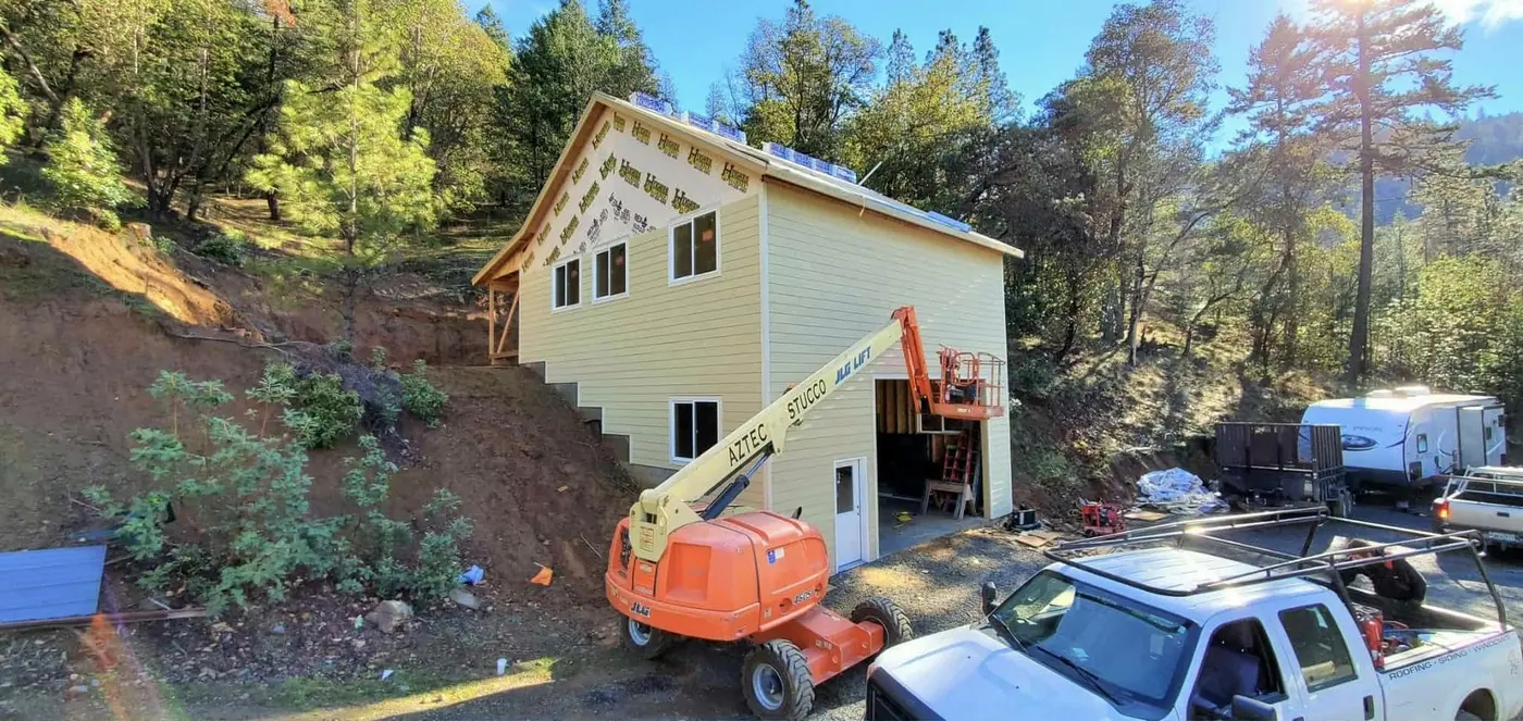 Siding installation underway on a hillside home with a boom lift on site, Next Gen Contracting in Southern Oregon