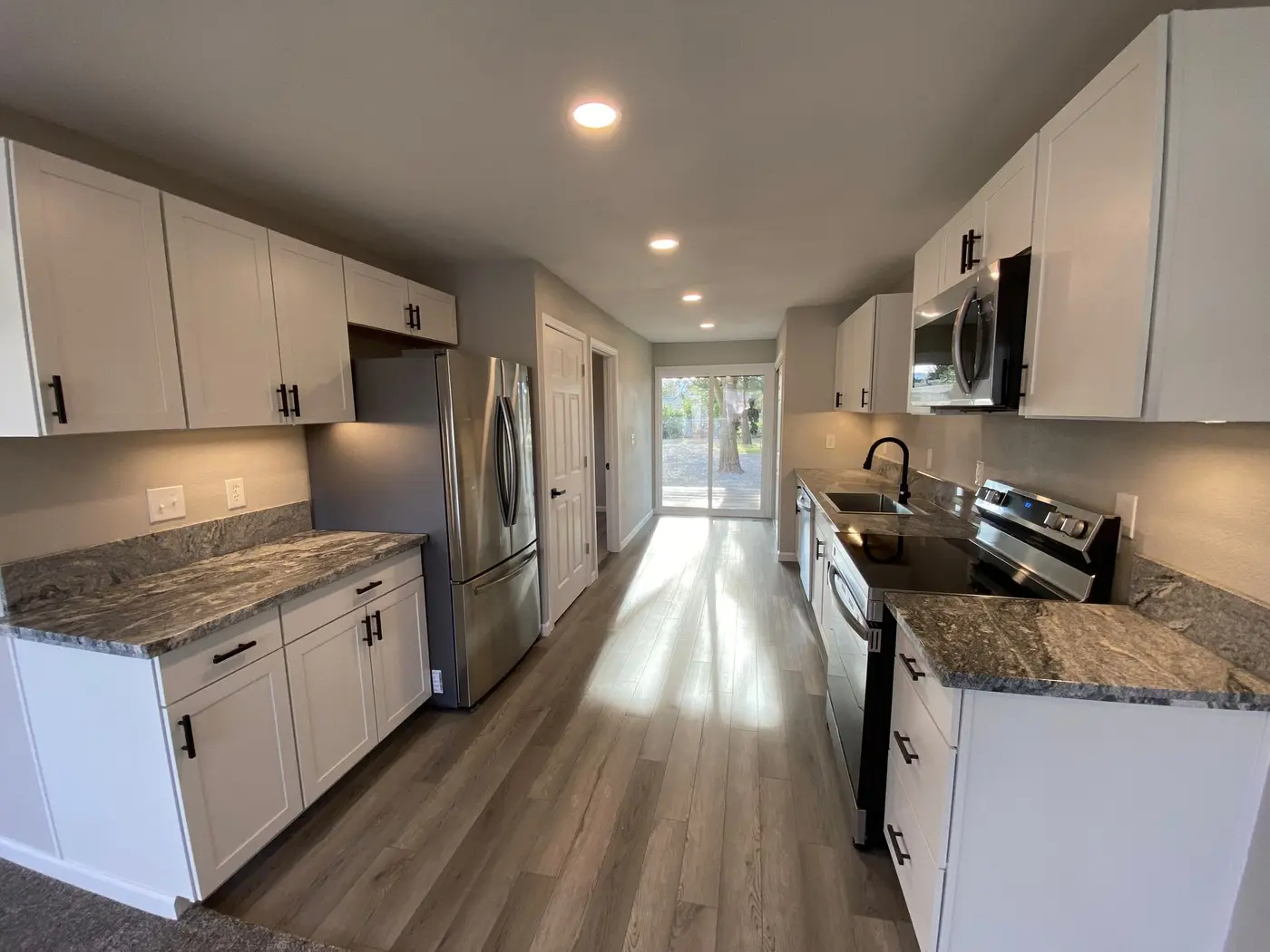 Remodeled galley kitchen with white shaker cabinets and stainless appliances by Next Gen Contracting in Southern Oregon